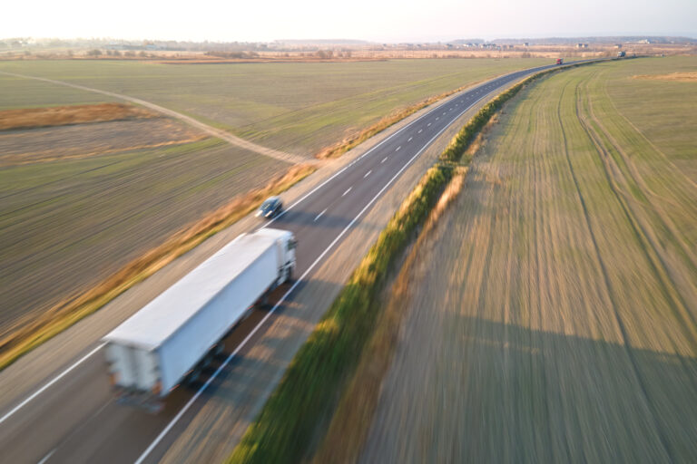 Aerial view of blurred fast moving semi-truck with cargo trailer driving on highway hauling goods in evening. Delivery transportation and logistics concept.
